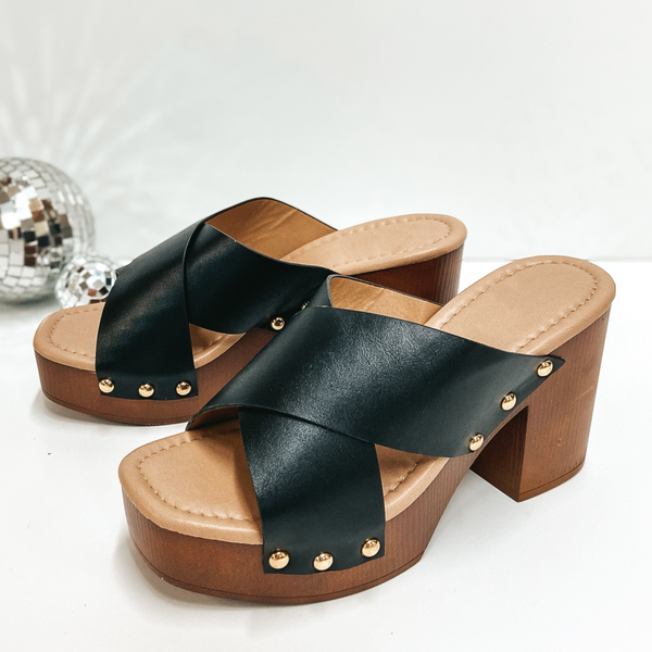 A pair of clog style heels with a black criss cross band. Pictured on white background with disco balls.
