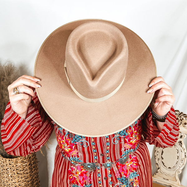 Model is holding a sand color rancher hat over her face.
