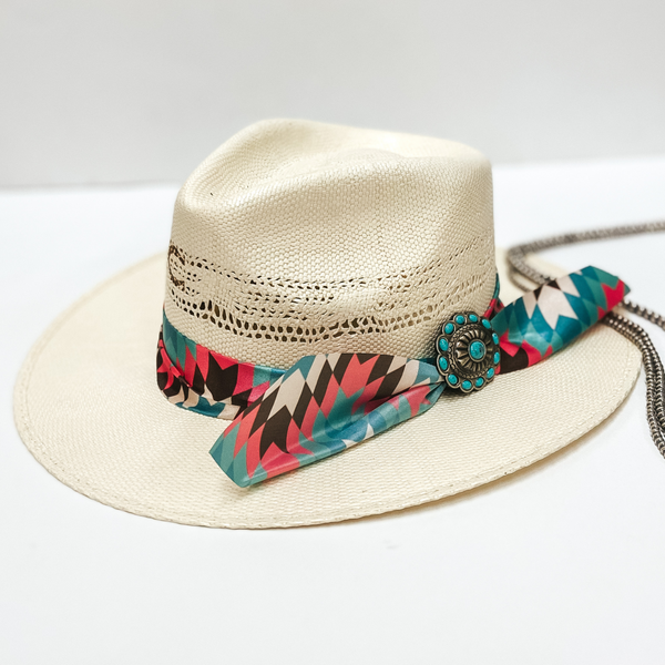 A light beige straw hat with a turquoise and pink ribbon band and a turquoise and silver concho. Pictured on white background with navajo pearls.