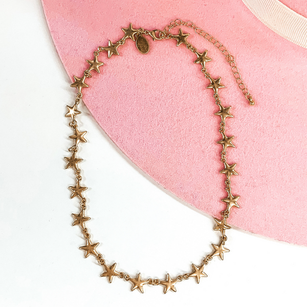 Gold star linked adjustable necklace. This necklace is pictured on a white and pink background.