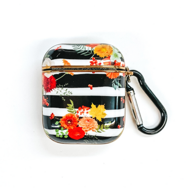 This airpod case has black and white horizontal stripes. There is also colored flowers throughout. This airpod case has a black and silver clip. This airpod case is pictured on a white background.