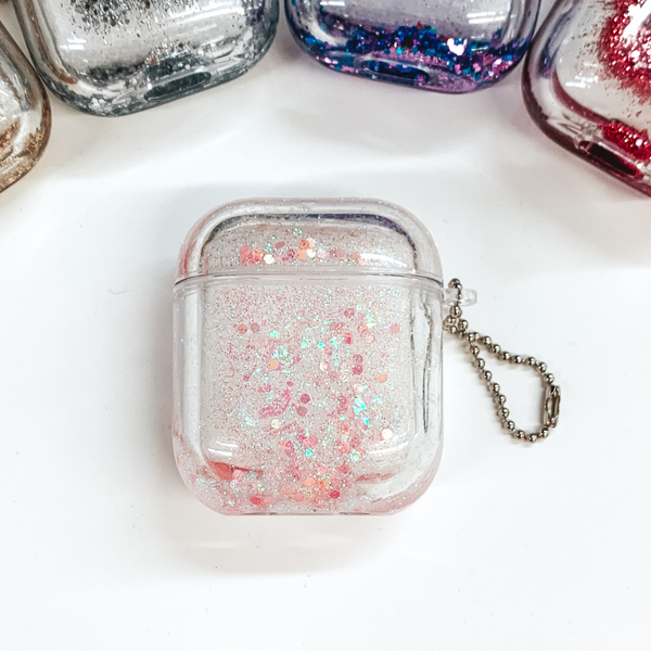 This is a clear airpod case filled with light pink, iridescent confetti inside the case. This case has a silver ball chain on one side. This case is pictured on a white background.