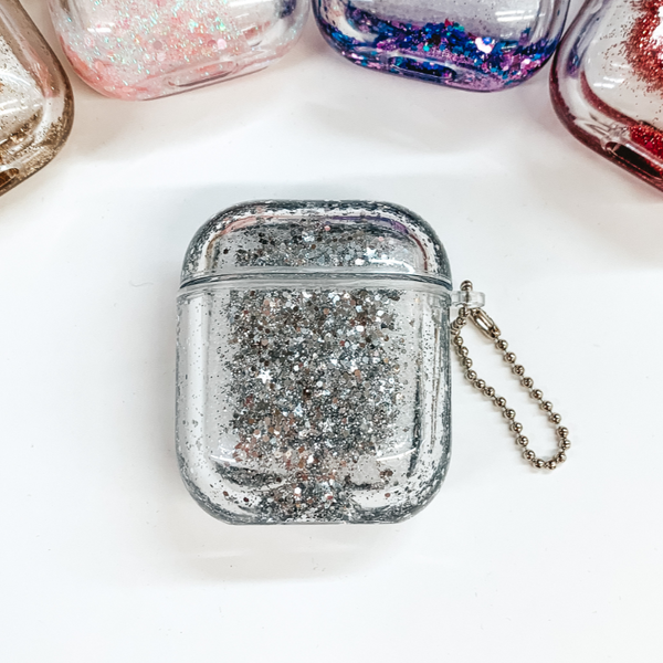 This is a clear airpod case filled with silver confetti inside the case. This case has a silver ball chain on one side. This case is pictured on a white background. 