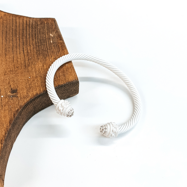 Cable bracelet with clear crystal cabochon ends in white. This bracelet is pictured on a white background and leaning on a piece of brown wood. 