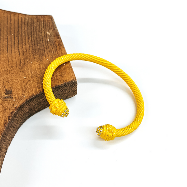 Cable bracelet with clear crystal cabochon ends in yellow. This bracelet is pictured on a white background and leaning on a piece of brown wood. 