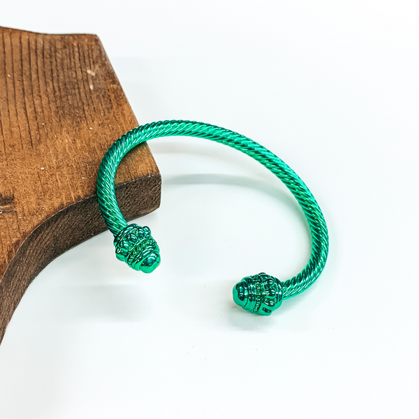 Cable bracelet with cabochon ends in metallic green. This bracelet is pictured on a white background and leaning on a piece of brown wood.