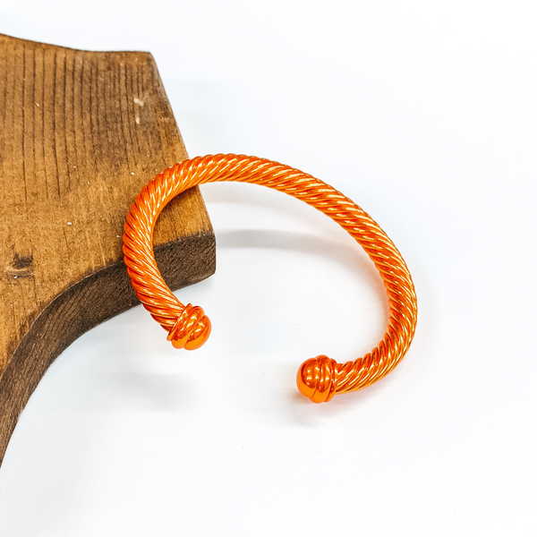 Cable bracelet with cabochon ends in metallic orange. This bracelet is pictured on a white background and leaning on a piece of brown wood. 