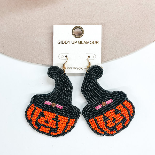 These are beaded pumpkin earrings that also have a black witch hat on top. The pumpkin also includes a jock o lantern face. These earrings are taken laying on a beige color hat brim and on a white background.     