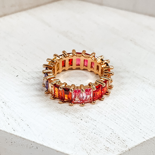 Gold ring with rectangle colored crystals around the entire ring. The crystals come in yellow, pink, red, garnet, and purple shades. This ring is pictured on a white background. 