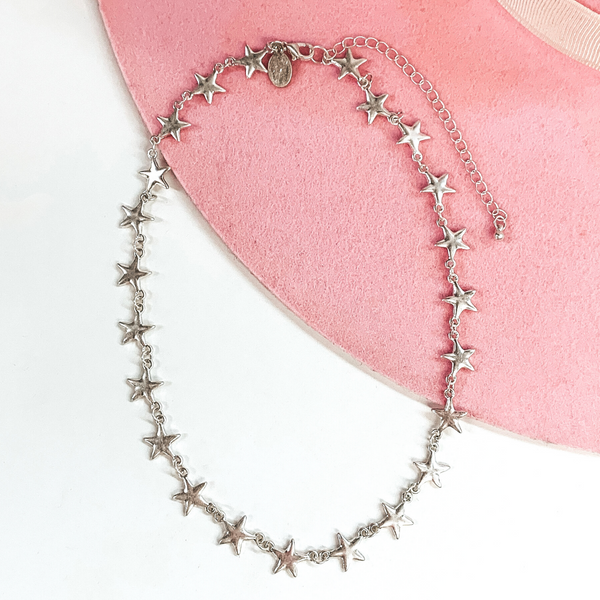 Silver star linked adjustable necklace. This necklace is pictured on a white and pink background. 