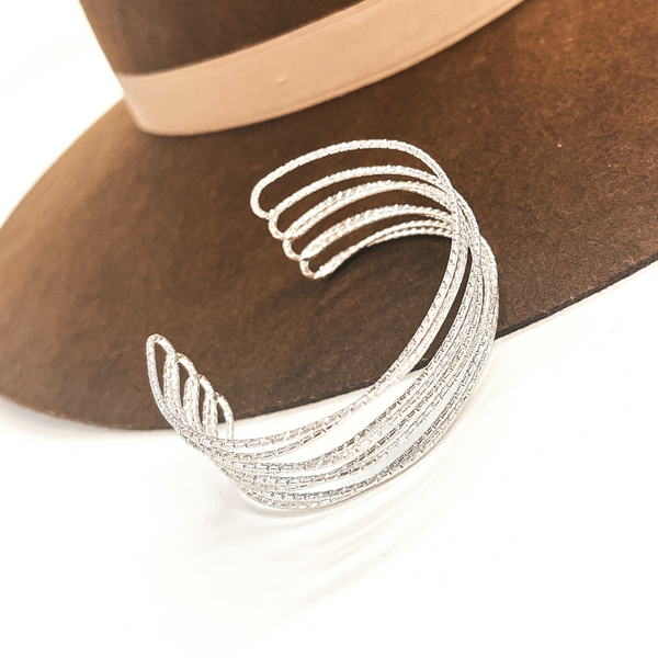 This is a silver cuff bracelet, there are eight layered textured wires.  This cuff bracelet is open ended. This bracelet is taken on a dark brown brim hat and on a white background.