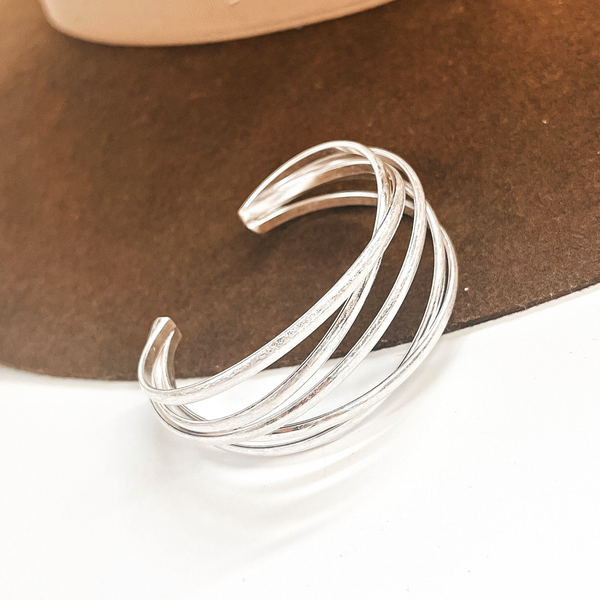 This is a silver metal cuff bracelet, there are five layers interwining with  an open end. This bracelet is taken on a dark brown brim hat  and on a white background.