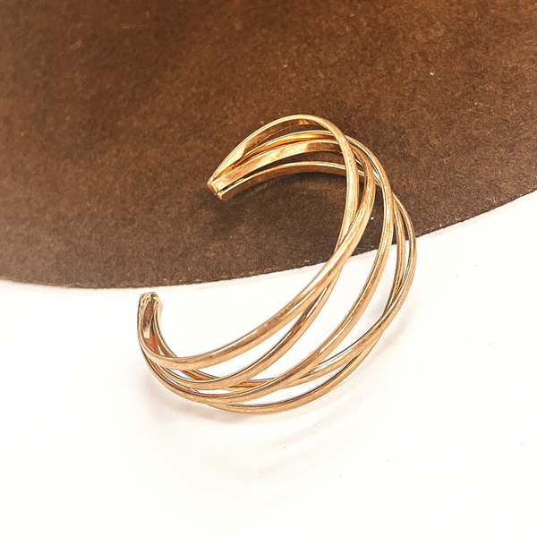 This is a gold metal cuff bracelet, there are five layers interwining with  an open end. This bracelet is taken on a dark brown brim hat  and on a white background.