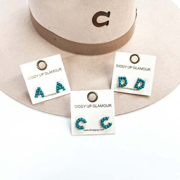 These are three pair of initial earrings with small turquoise stones in  a silver setting. From left to right; A,C,D. These earrings are placed  on a white thekitchenapproach card, they are laying on a beige, felt,  Charlie 1 Horse hat and on a white background.