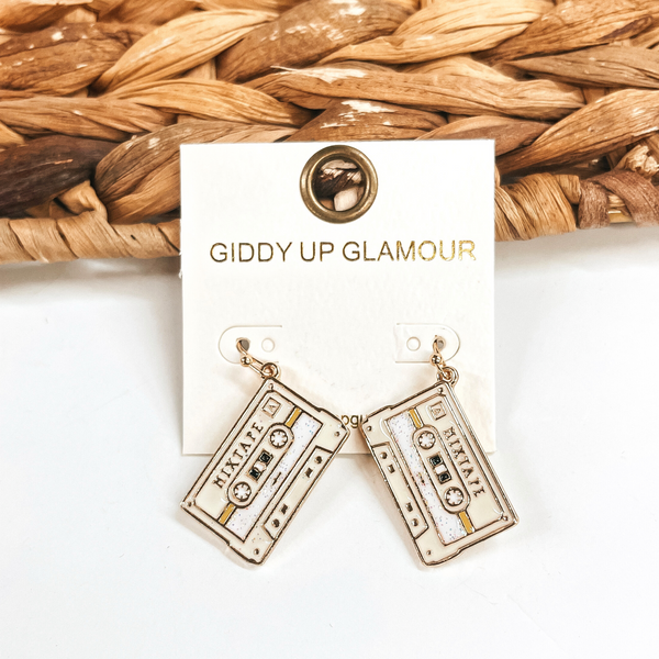 These are ivory mixtape shaped earrings in a gold setting with glitter in the  center. These earrings are taken leaning up against a brown woven slate and on a white  background.