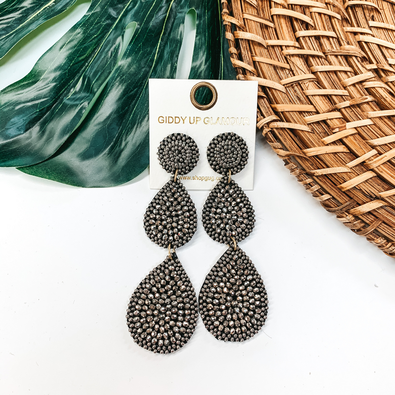 Charcoal grey tiered beaded earrings pictured on white background with a basket and palm leaf.